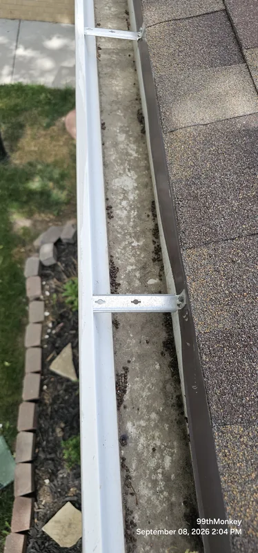 Close-up along an open gutter beside an asphalt shingle roof